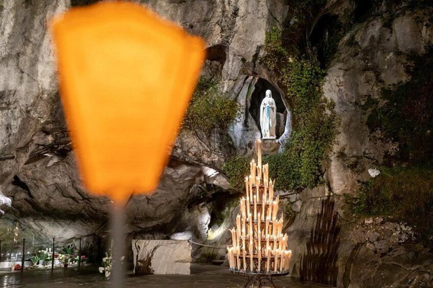 Interno di una grotta con una statua, un'illuminazione a candela e una cascata. 2