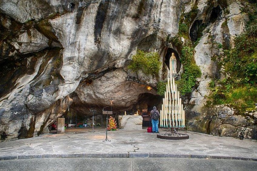 L'ingresso di una grotta con una statua di una figura religiosa, una persona in piedi nei pressi dell'ingresso e un piccolo santuario con candele. 5
