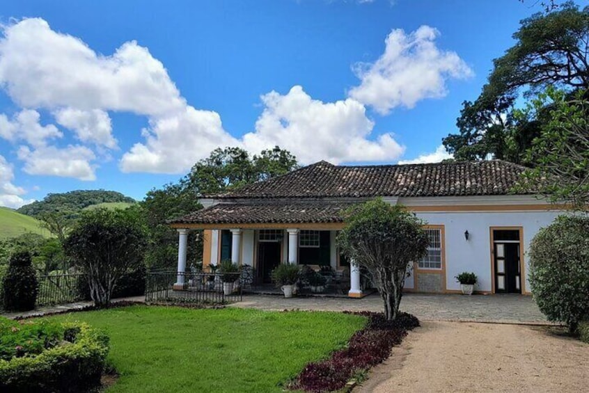 A colonial-style house with a tiled roof, surrounded by a well-maintained garden and a clear blue sky. 4