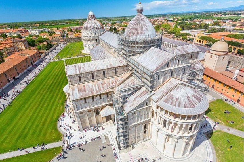 The Pisa Cathedral with its famous leaning dome, surrounded by a green lawn and a crowd of visitors. 2