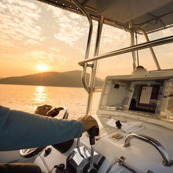 A person steering a boat at sunset with a view of the water and distant land. 2