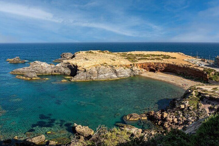 A coastal landscape with clear turquoise waters, rocky formations, and a sandy beach. 4