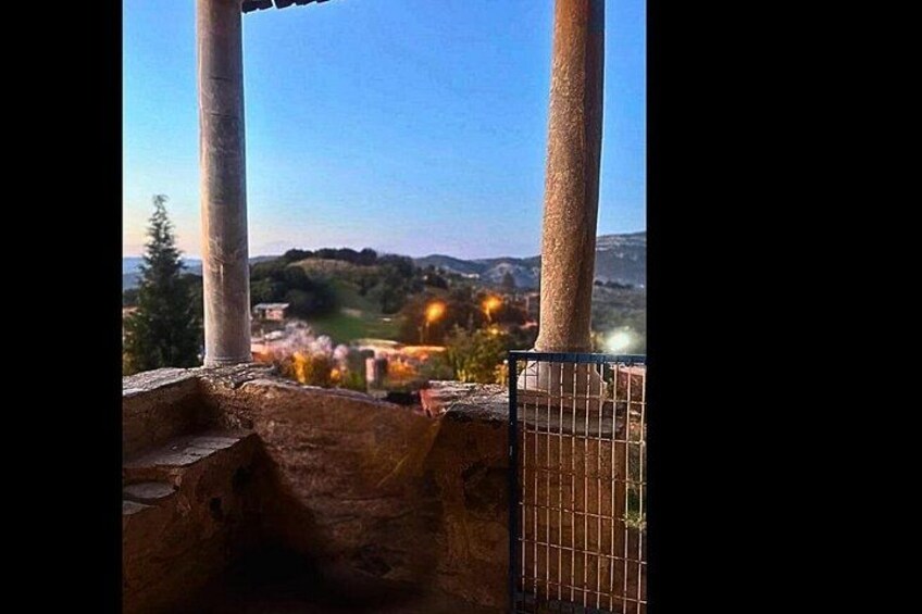 A view of a landscape with a metal fence, a stone structure, and a distant village with lights. 4
