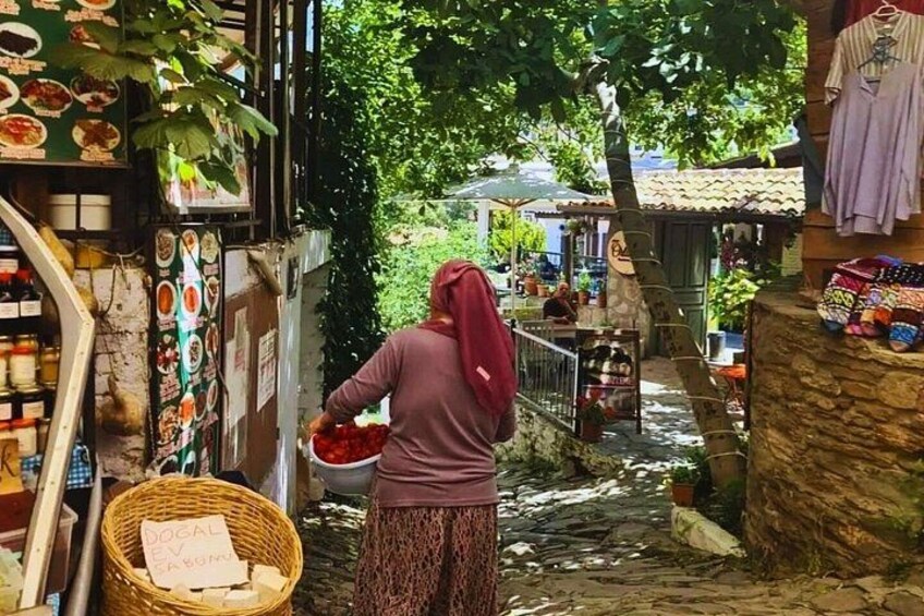 A narrow alley with a woman carrying a basket, surrounded by various shops and hanging clothes. 5