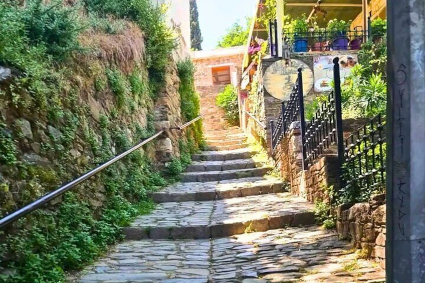 A stone staircase leading up a hill, flanked by greenery and a building with a balcony. 2