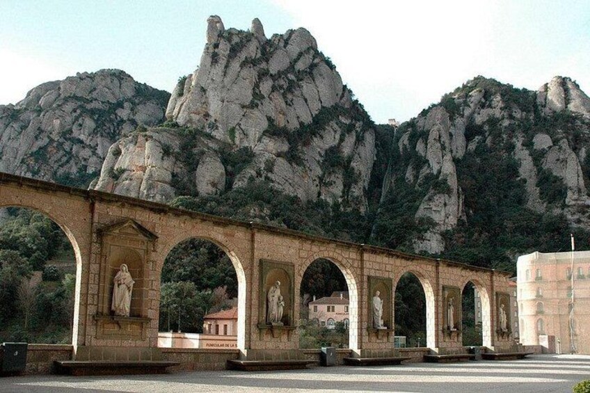 Un pont de pierre orné de statues, une chaîne de montagnes en arrière-plan et un bâtiment visible au loin. 2