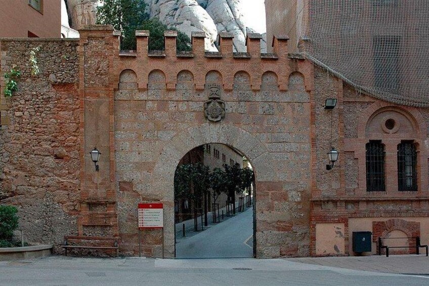 Une arche en pierre surmontée d’un motif décoratif, une rue avec un banc, et un bâtiment doté de fenêtres en arc de cercle. 5