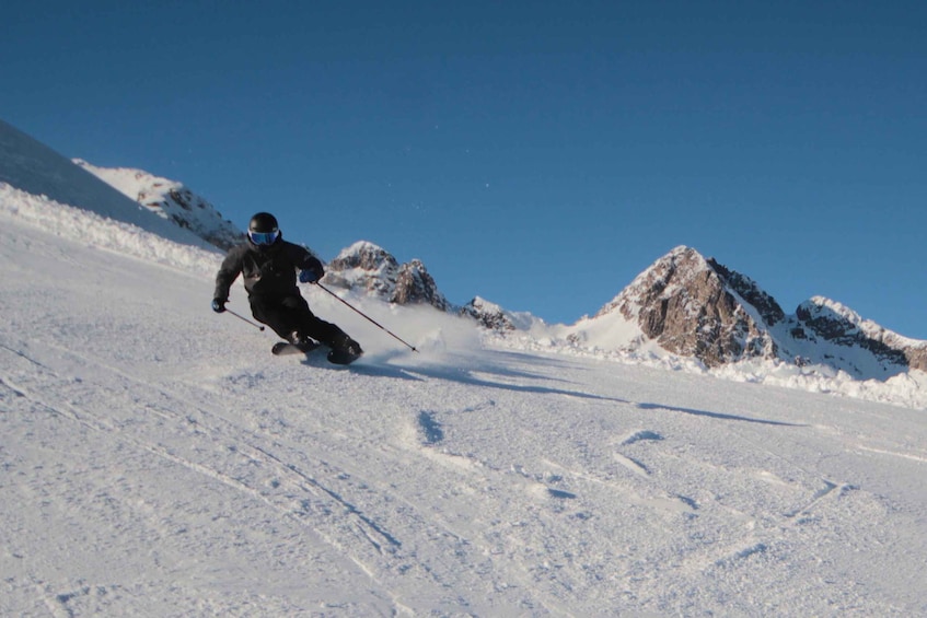 A skier descending a snowy slope with rocky mountains in the background. 5