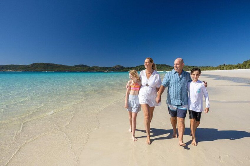 En familie på fire på en sandstrand med krystalklart turkis vand og fjerne, grønne bakker. 5