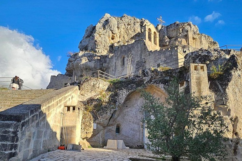 A historical building with a staircase leading up to it, set against a rocky cliff. 2