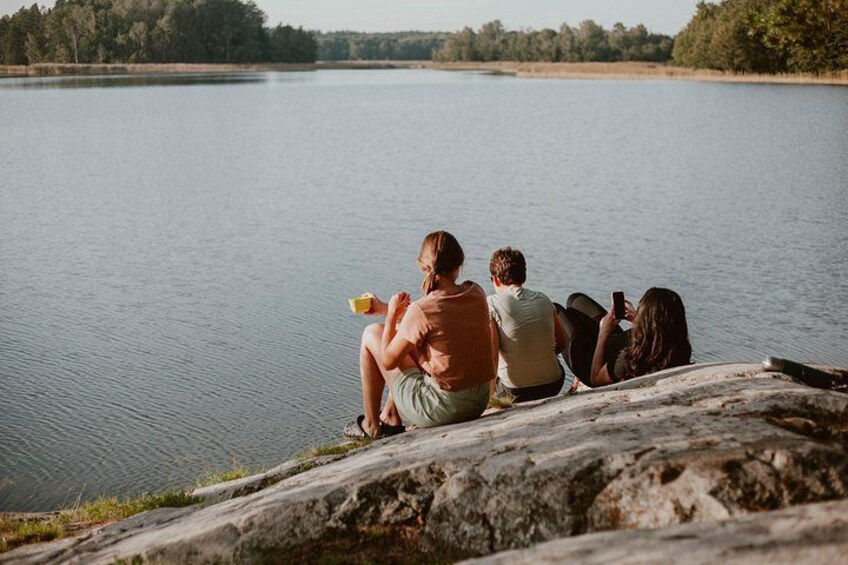 A group of people sitting on a rock by a calm lake. 3