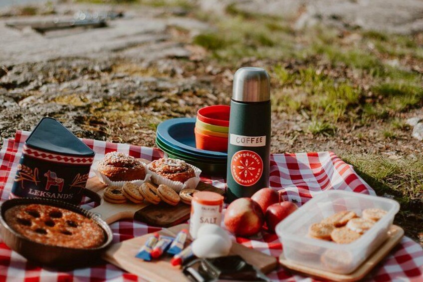 A picnic setup with food items, a thermos, and a container on a checkered cloth outdoors. 5