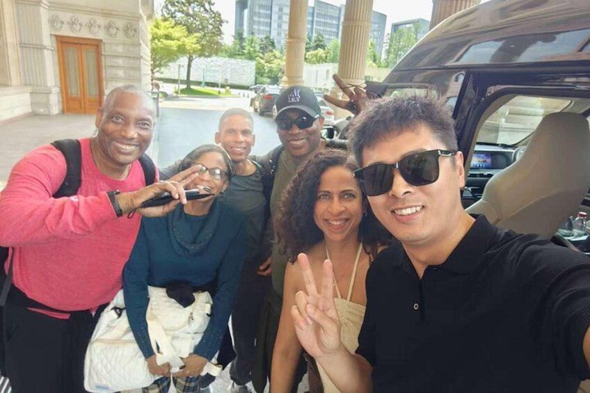 A group of people posing for a selfie in front of a building with columns and a parked car. 3
