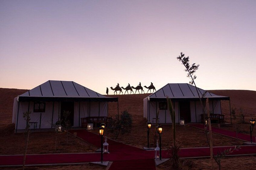 Two tents with red carpets, a camel caravan, and desert landscape. 4