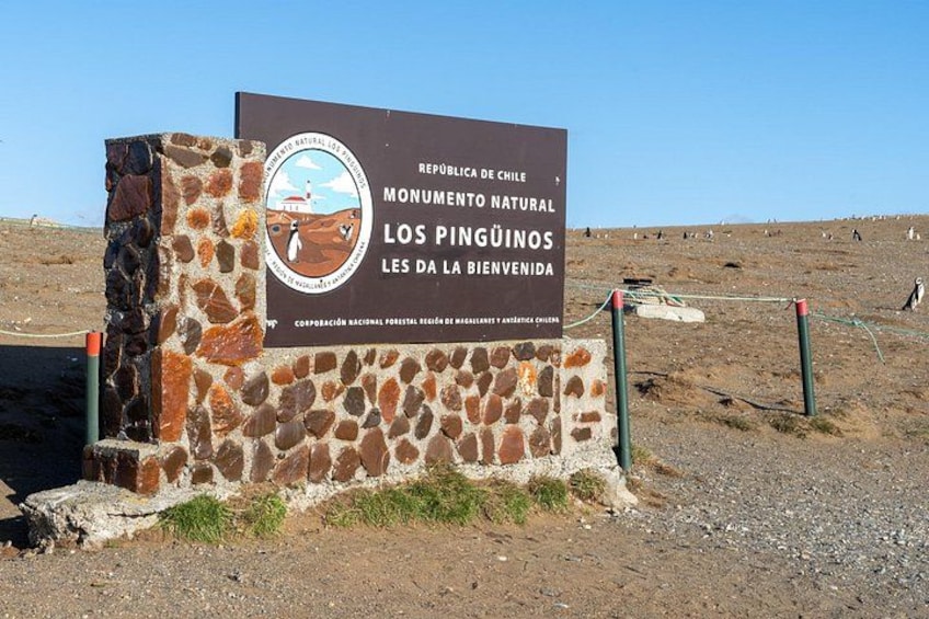Un panneau indiquant le « Monument naturel de Los Pingüinos » au Chili, avec un ciel dégagé et un paysage aride en arrière-plan. 2