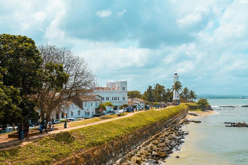 A coastal town with a lighthouse, white buildings, and a paved walkway along the shore. 2
