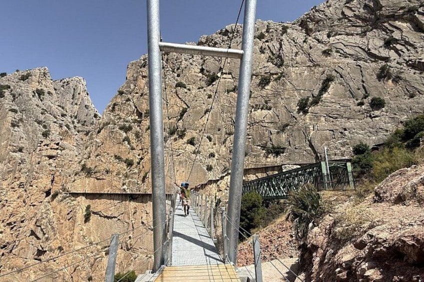 A metal bridge with a metal railing, rocky cliffs, and sparse vegetation. 4