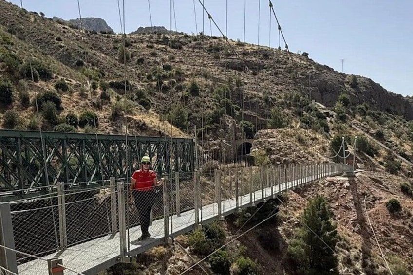 A pedestrian bridge with a metal railing, a hilly landscape, and a clear sky. 5