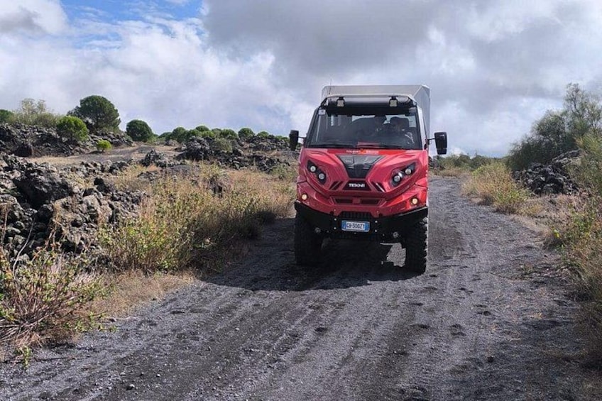 A red off-road vehicle on a dirt path with rocky terrain and sparse vegetation. 1