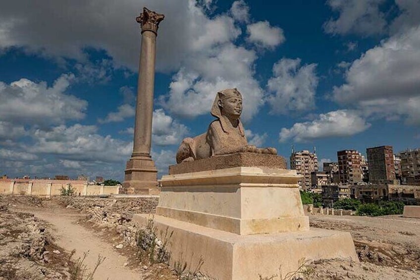 A sphinx statue and a tall column in an open area with a cityscape in the background. 5