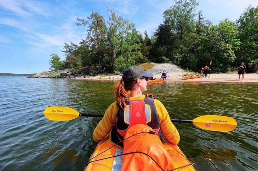 Una persona remando en kayak por un río, con árboles y otros kayakistas al fondo. 1
