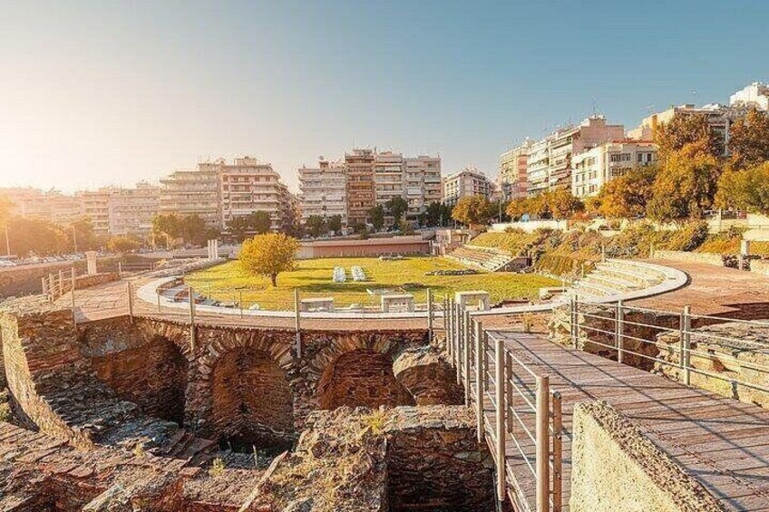 An ancient amphitheater with ruins, a grassy area, and modern buildings in the background. 4
