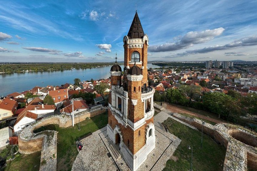 Una torre histórica con un reloj, rodeada por un foso y una ciudad con edificios de techo rojo. 4