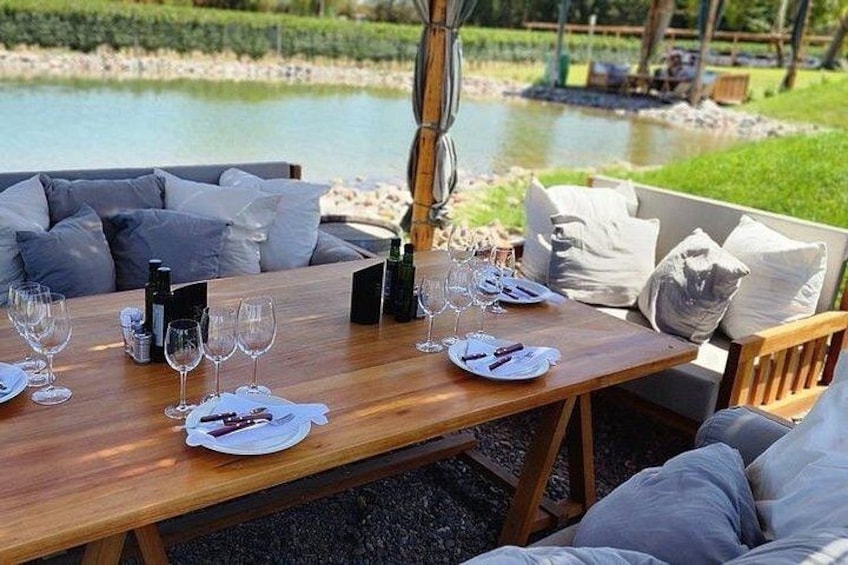 An outdoor dining table set with wine glasses, plates, and cutlery, surrounded by a grassy area and a body of water. 5