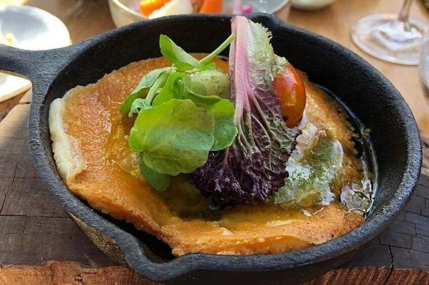 A skillet with a golden-brown pancake, topped with greens and a cherry tomato. 3