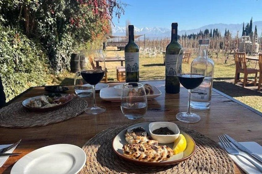 A dining table set outdoors with wine bottles, glasses, and plates of food. 2