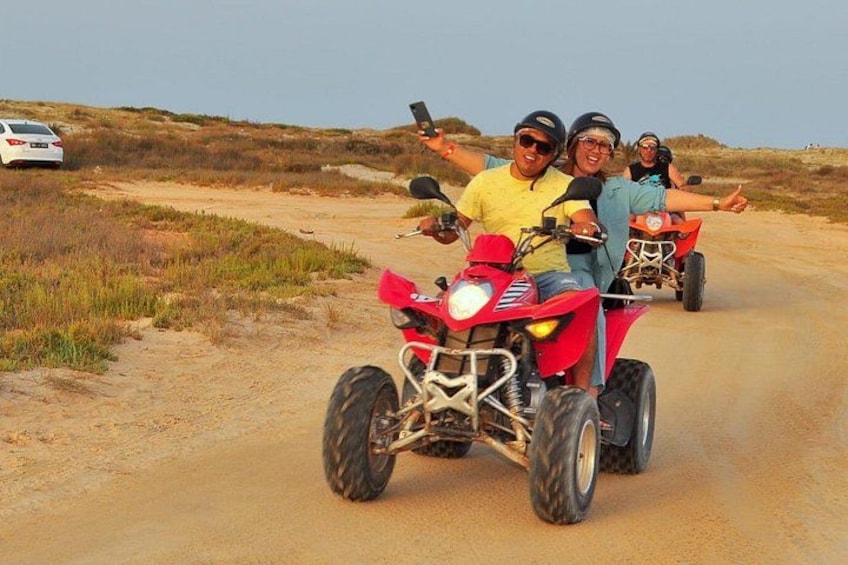 Trois personnes sont à bord d’un quad rouge sur un chemin de terre où la végétation est clairsemée. 3