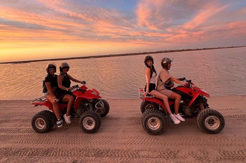 Deux personnes sur des quad rouges sur une plage de sable, avec une étendue d’eau en arrière-plan. 2