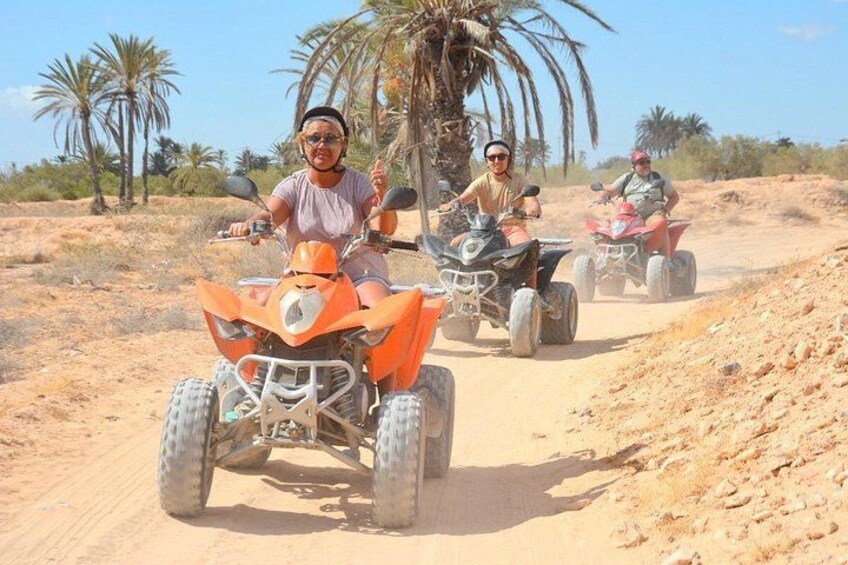 Trois personnes conduisent des quads sur un sentier sablonneux, avec des palmiers en arrière-plan. 4