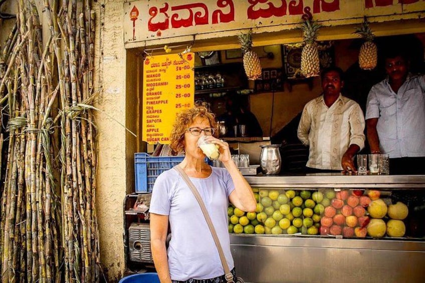 A person drinking from a cup at a fruit stand with various fruits displayed. 2