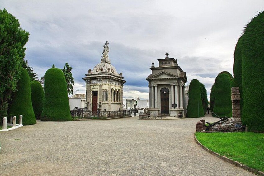 A cemetery with two ornate chapels, trimmed hedges, and a clear sky. 3