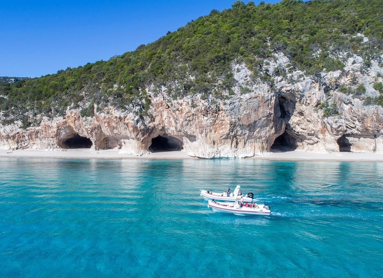 A coastal scene with clear turquoise waters, a rocky cliff with caves, and a boat with passengers. 2