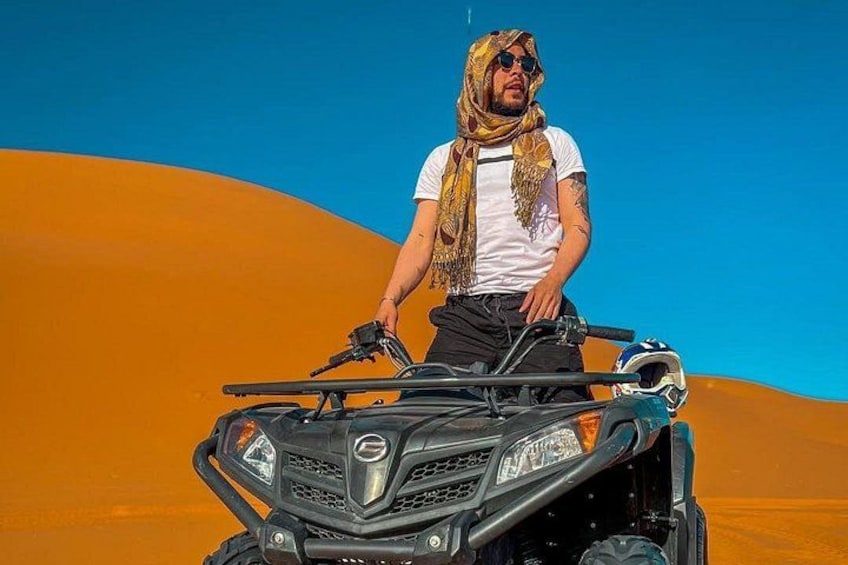 Une personne conduisant un quad dans un désert, avec des dunes de sable en arrière-plan. 2