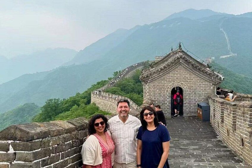 Een groep mensen staat op een stenen muur met uitzicht op de Chinese Muur en bergen op de achtergrond. 5