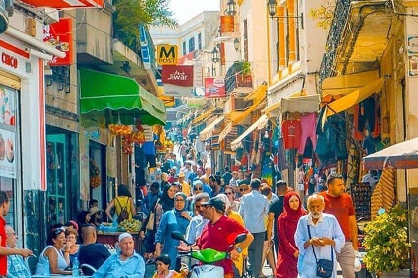 A crowded street lined with shops and people walking. 1
