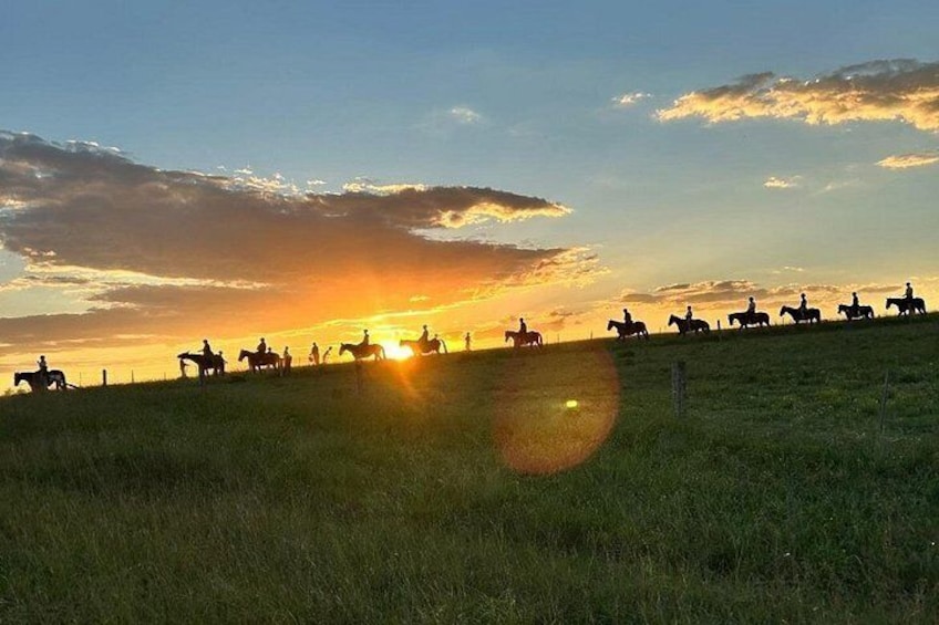 Un coucher de soleil sur un champ herbeux, avec les silhouettes de personnes à cheval. 1