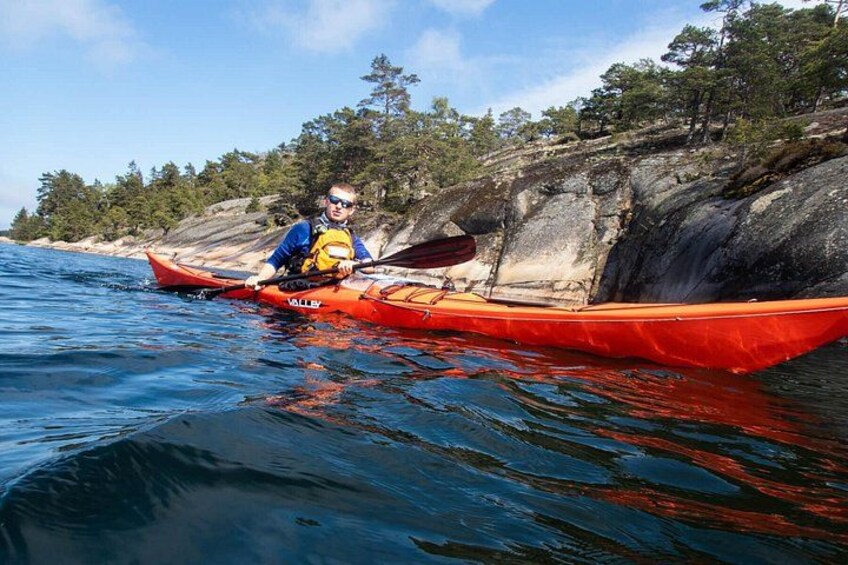 A person kayaking on a calm body of water with a rocky shoreline and trees in the background. 5