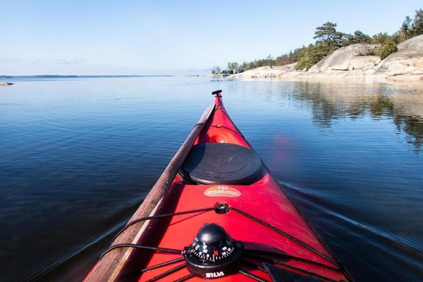 A red kayak on calm water with a rocky shoreline and trees in the background. 3