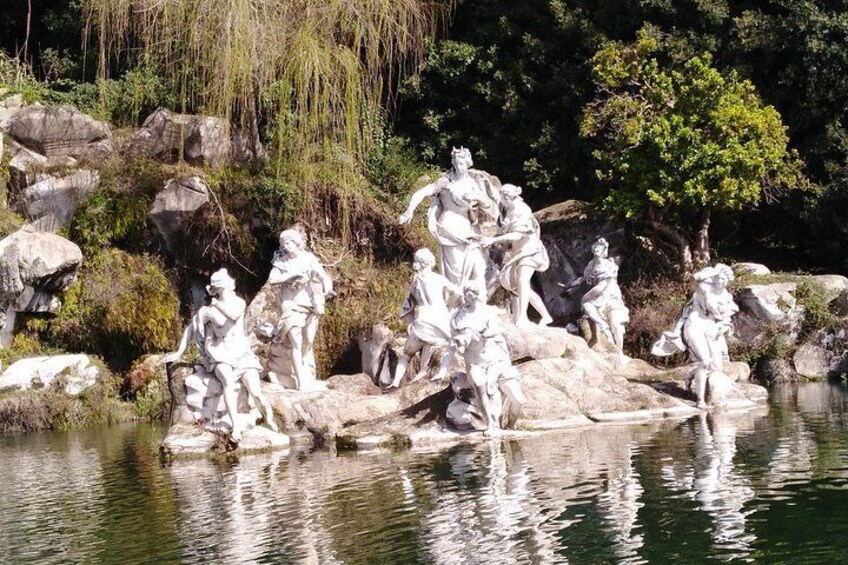 Eine Steinskulptur von Figuren an einem Gewässer, umgeben von Felsen und Grünpflanzen. 4