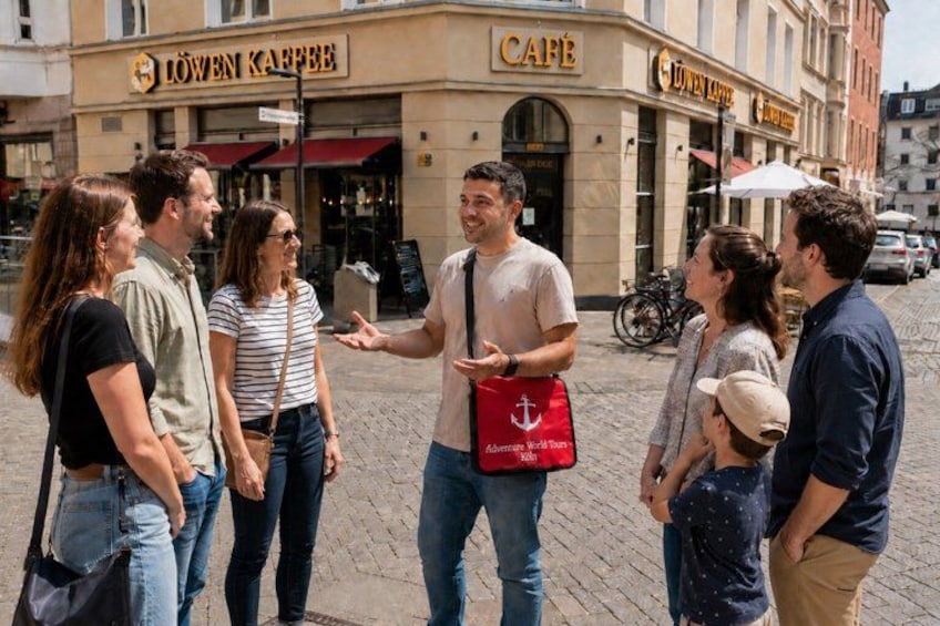 A group of people standing on a cobblestone street in front of a café named 'Löwen Kaffee'. 4