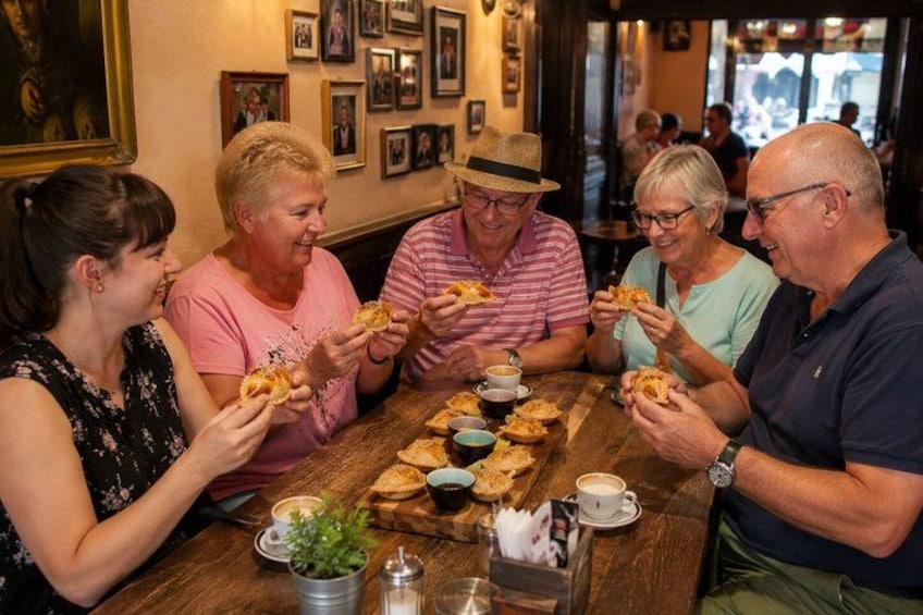 A group of people sitting around a wooden table, eating pastries and drinking coffee. 1