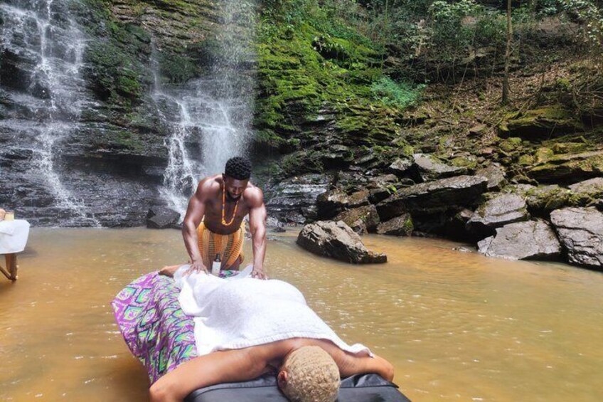 A person receiving a massage in a natural setting with a waterfall in the background. 3