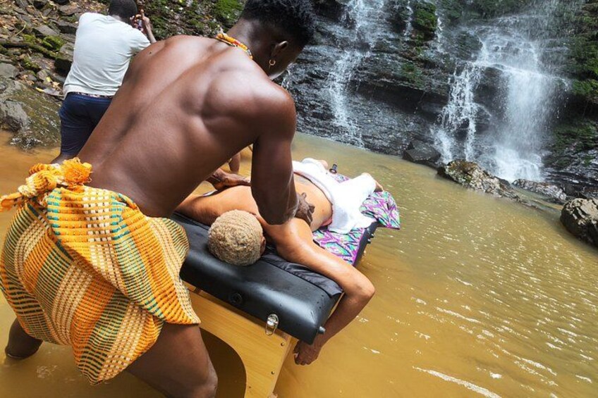 A person receiving a massage in a natural setting with a waterfall in the background. 2