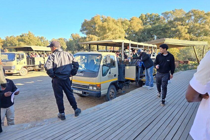A wooden boardwalk with people walking, a parked SUZUKI truck, and a covered area with people. 3
