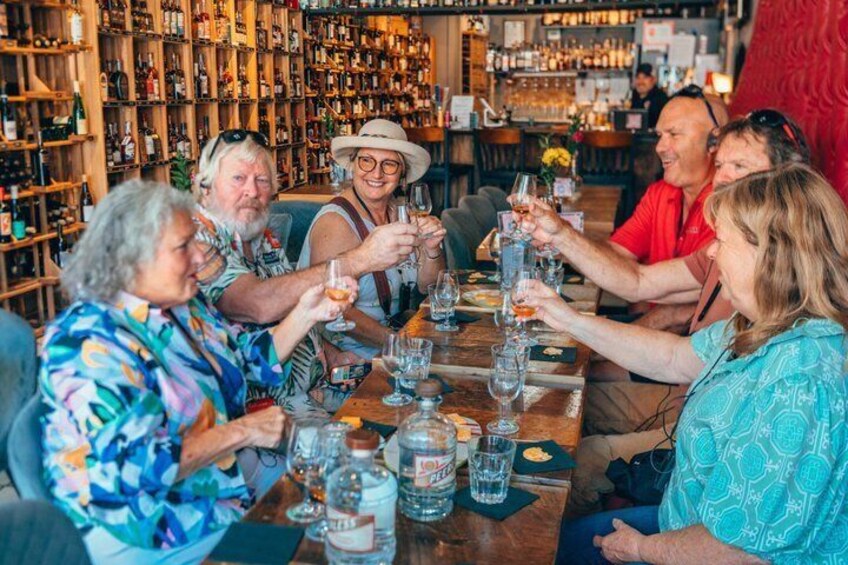 A group of people toasting at a bar with a variety of bottles and glasses on the table. 5