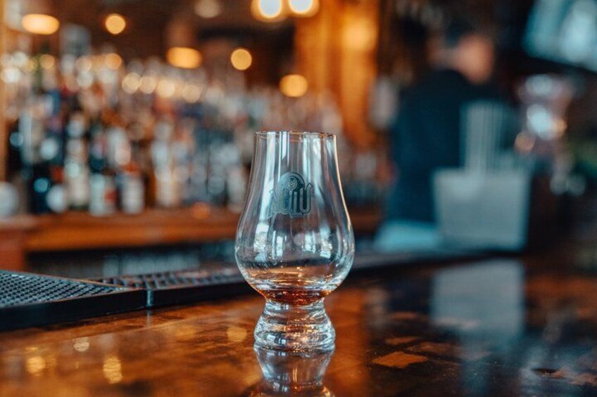 A clear glass on a bar counter with a blurred background of bottles and a person. 4